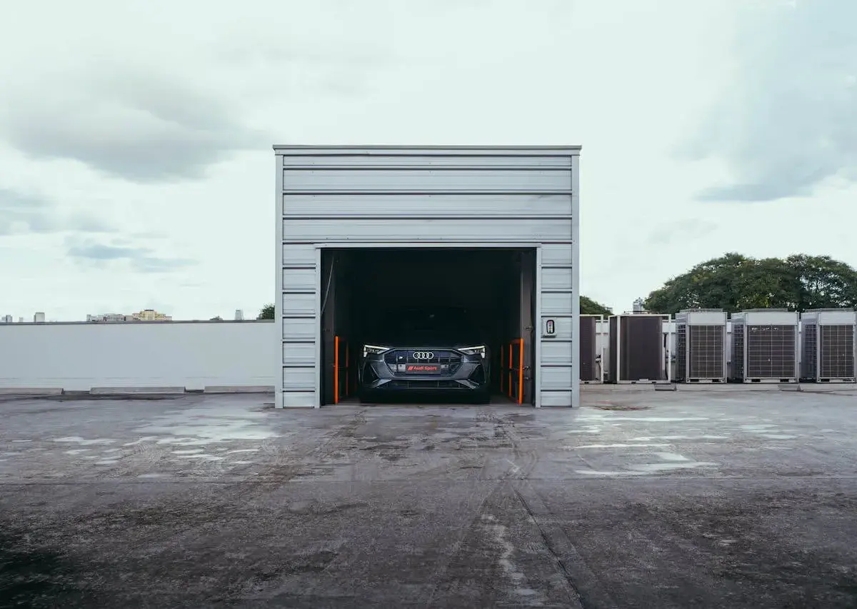 Classic car parked inside outdoor storage unit with roll-up door open.