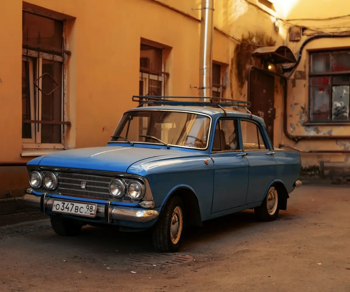 Vintage blue sedan parked in a courtyard beside older residential buildings.
