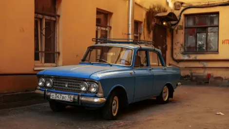 Vintage blue sedan parked in a courtyard beside older residential buildings.