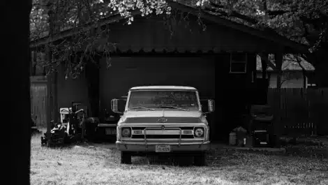 Vintage pickup truck parked in covered outdoor car storage shed.
