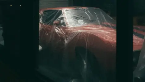 Classic car covered with plastic sheeting inside a dark garage