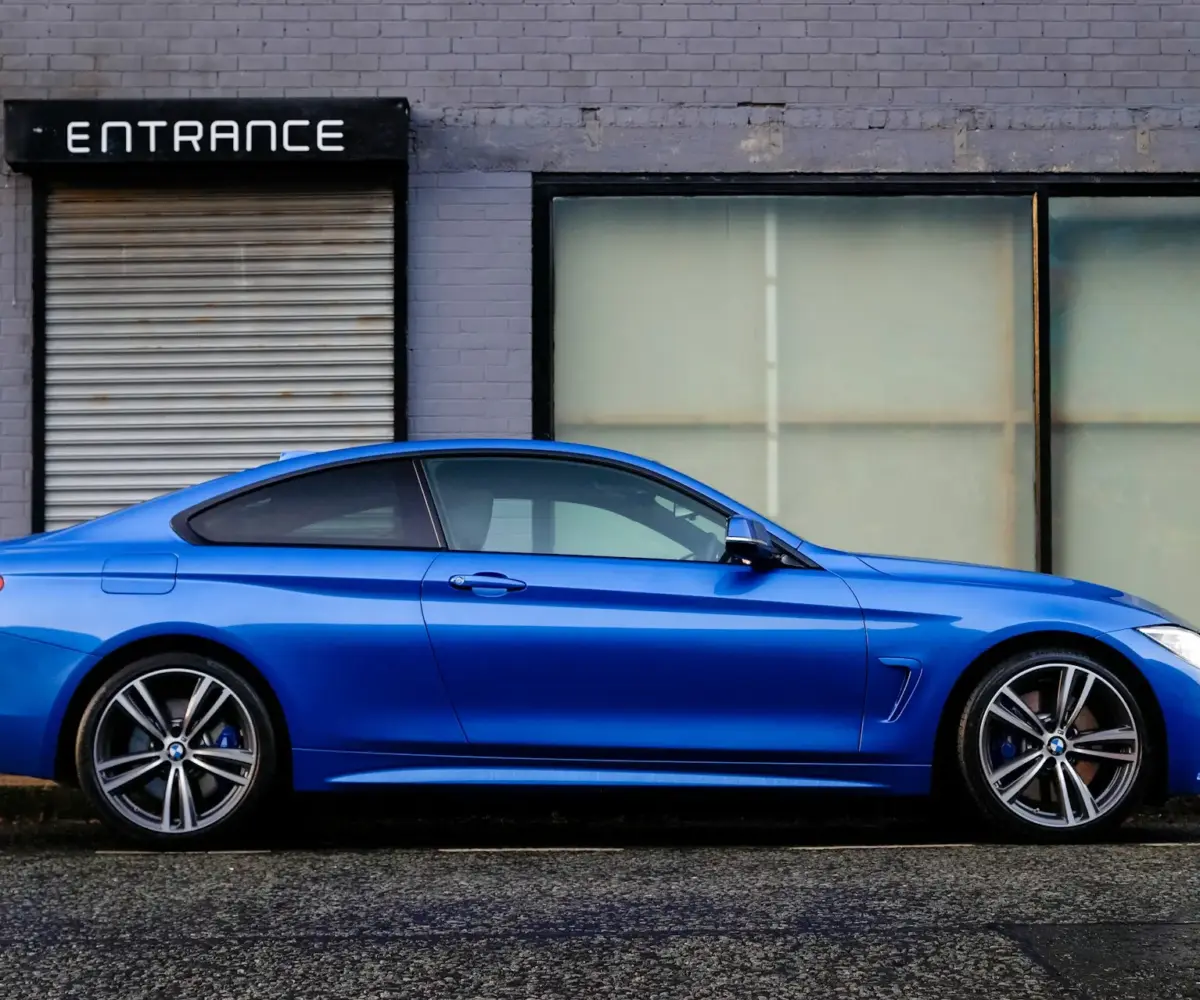 Blue sports car parked on a city street in front of a building entrance.