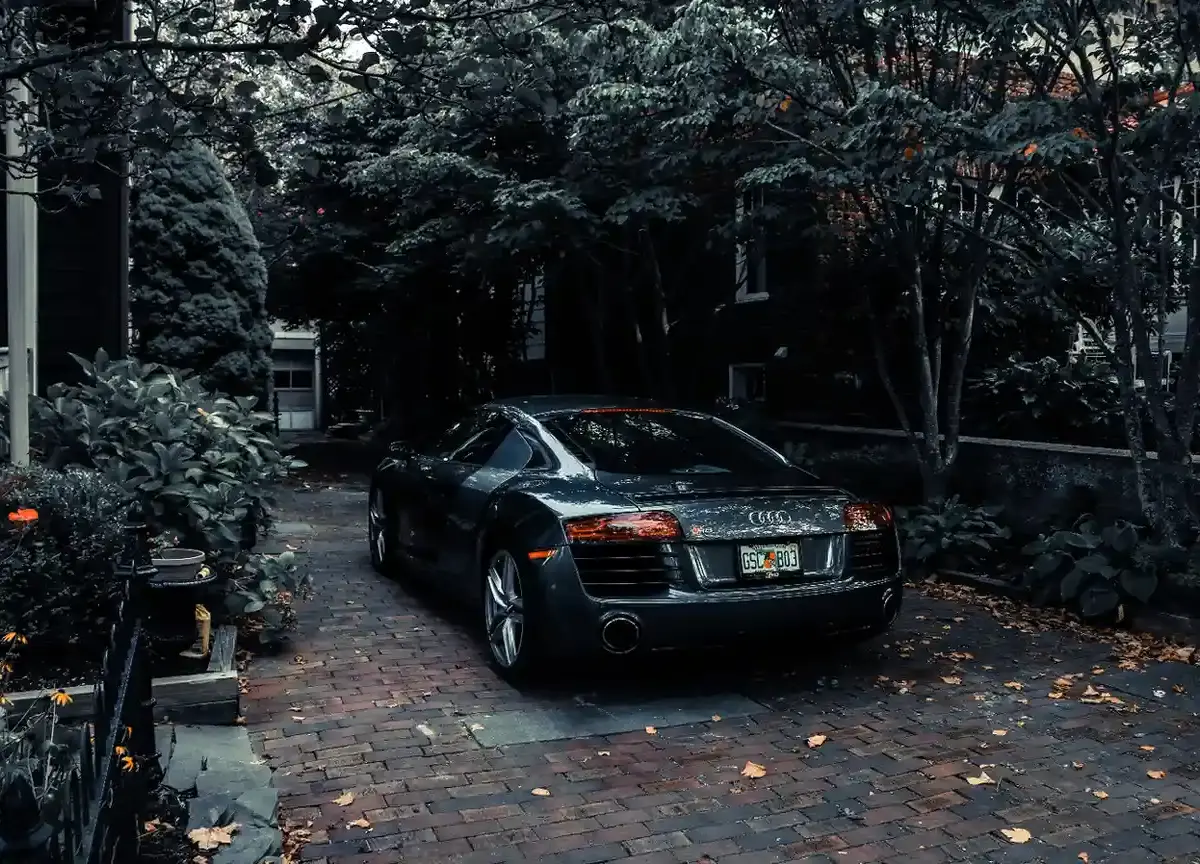 Car parked on a private garden driveway surrounded by trees and landscaping beside a residential home.