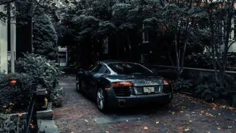 Car parked on a private garden driveway surrounded by trees and landscaping beside a residential home.