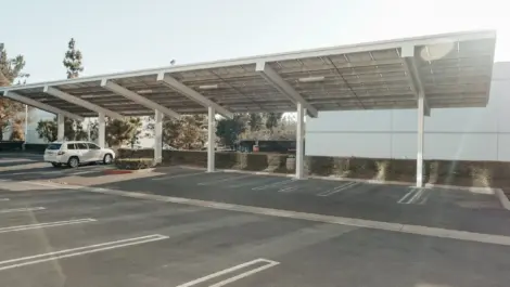 Covered outdoor parking structure with solar panel roofing and parked cars, illustrating a sheltered alternative to street parking.