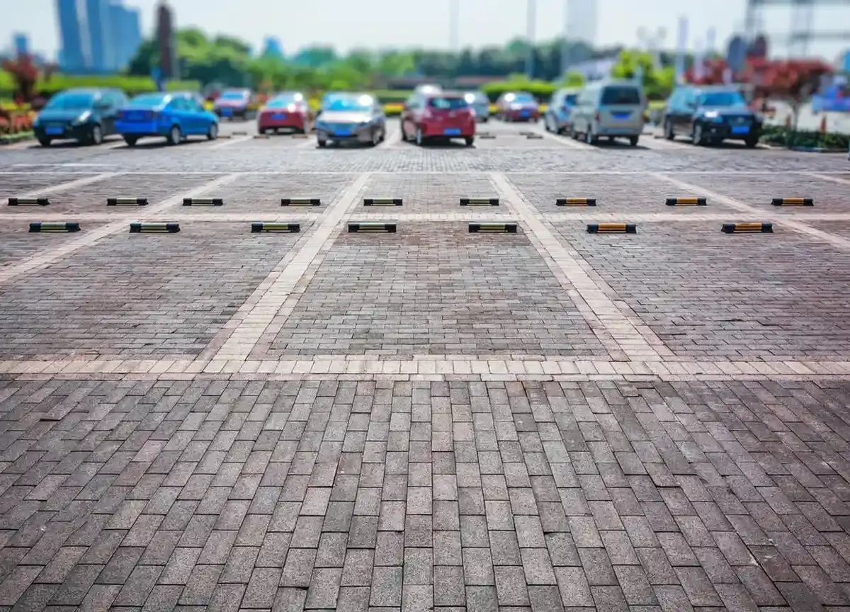 Open outdoor parking lot with multiple parked cars and empty parking spaces marked by wheel stops.