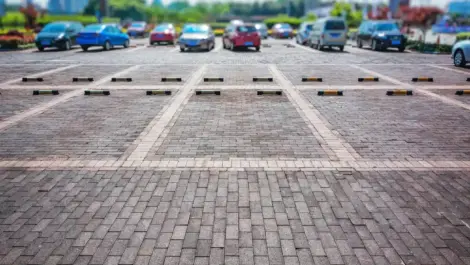Open outdoor parking lot with multiple parked cars and empty parking spaces marked by wheel stops.