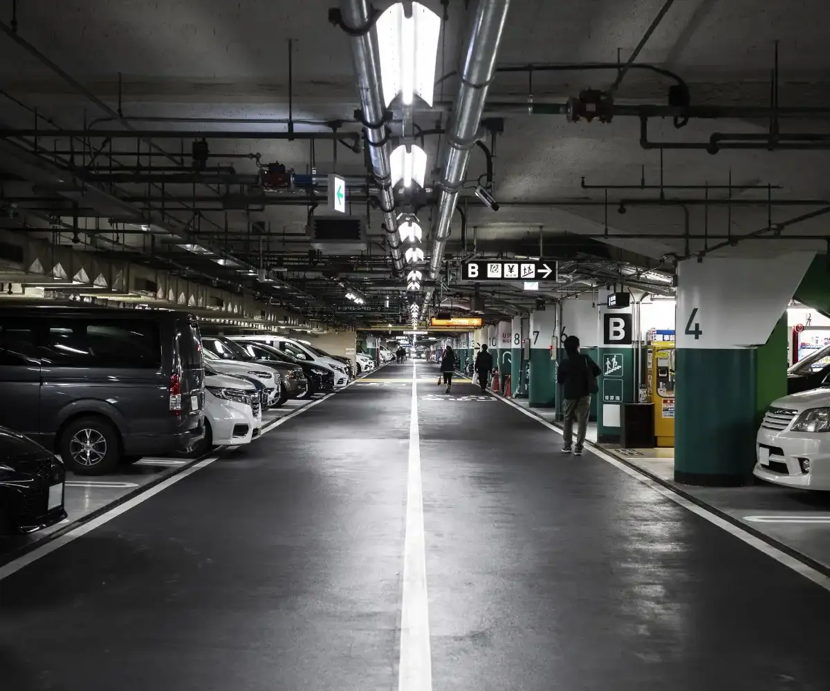 Underground parking garage with rows of parked cars, overhead lighting, and directional signs marking parking sections.