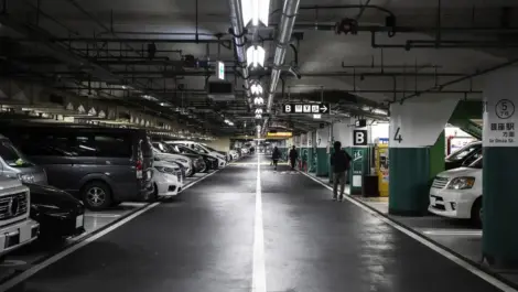 Underground parking garage with rows of parked cars, overhead lighting, and directional signs marking parking sections.