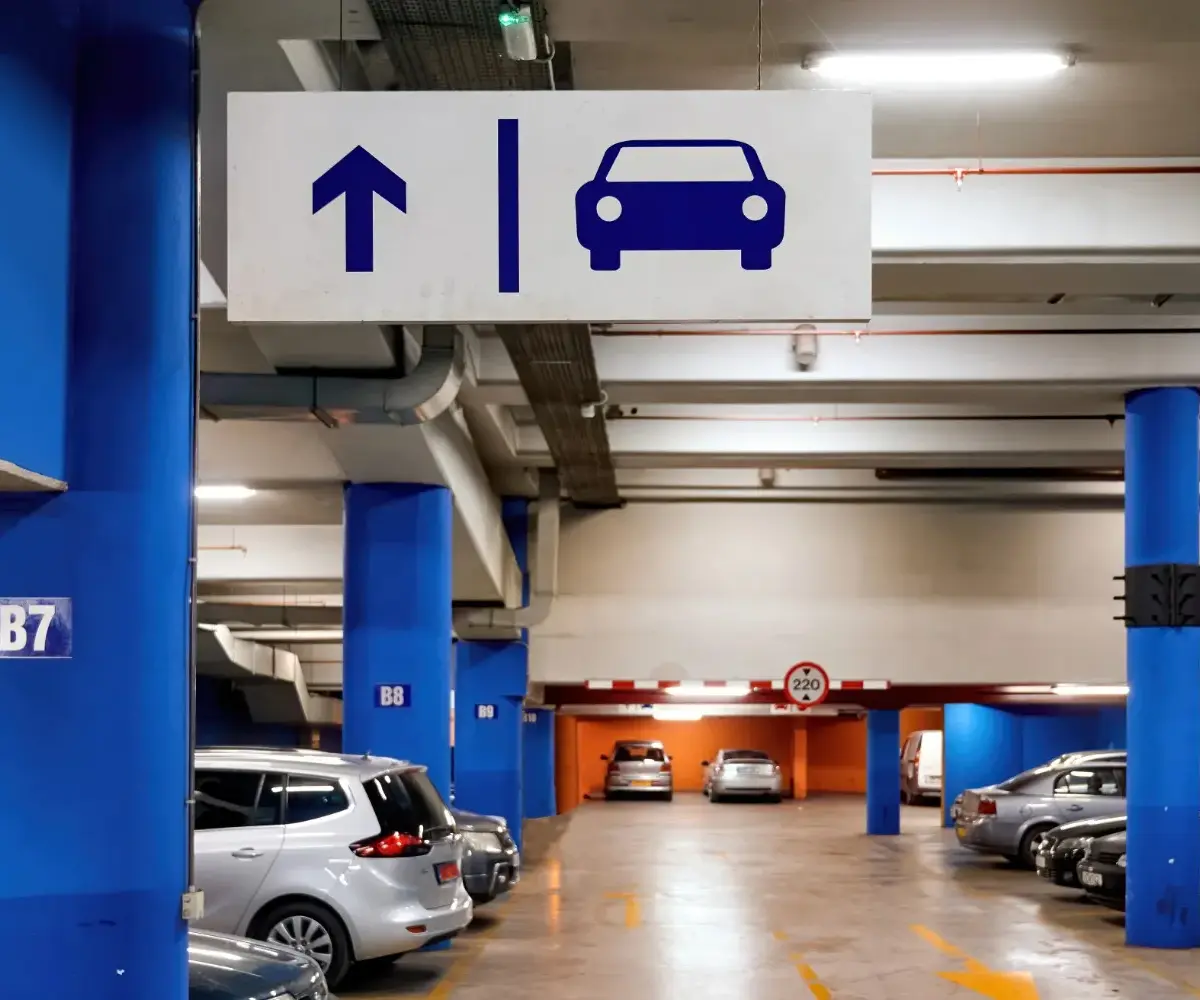 Underground parking garage with directional sign showing straight ahead arrow and car symbol, with several parked vehicles and blue support pillars.