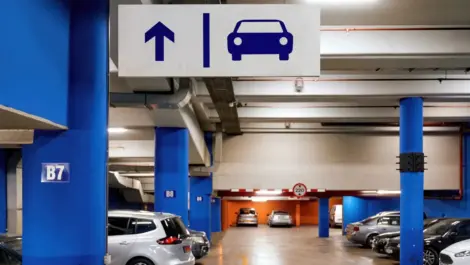 Underground parking garage with directional sign showing straight ahead arrow and car symbol, with several parked vehicles and blue support pillars.