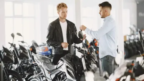 Motorcycle buyer receiving keys from a seller in a showroom, highlighting ownership transfer and post-purchase handling