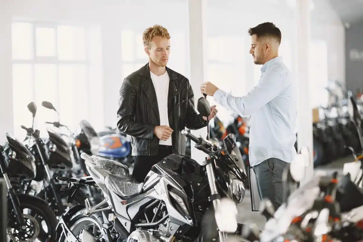 Motorcycle buyer receiving keys from a seller in a showroom, highlighting ownership transfer and post-purchase handling