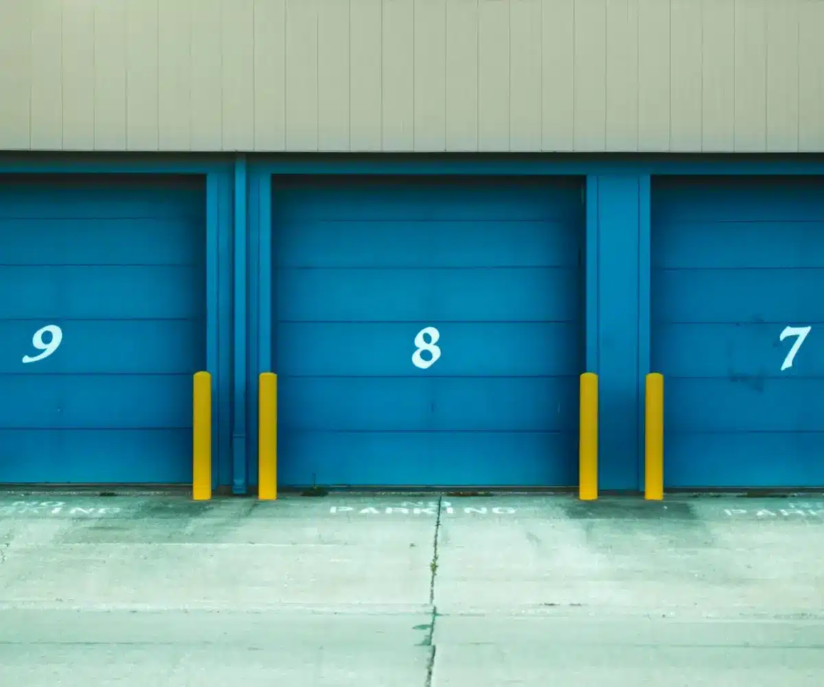 Storage facility with blue roll-up doors and concrete driveway.
