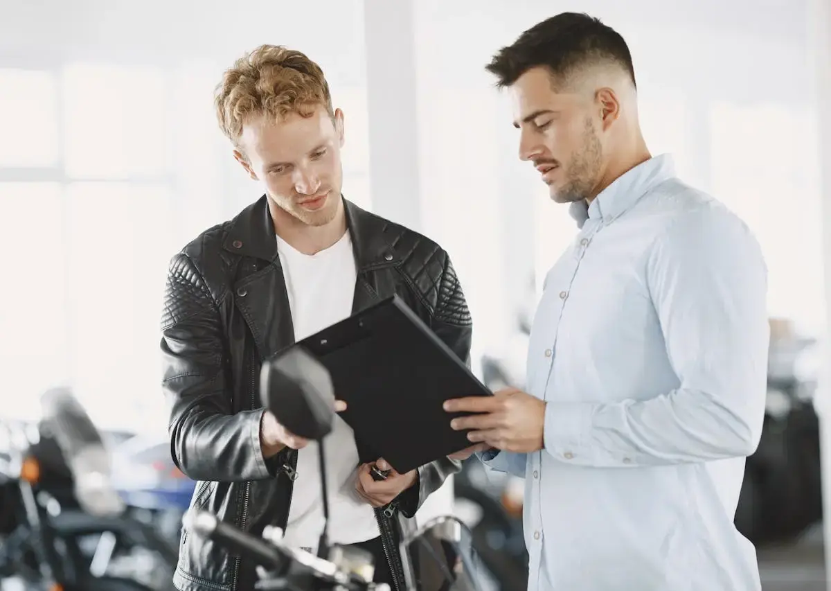 Two men reviewing motorcycle storage or insurance documents beside a bike, discussing coverage and protection options.