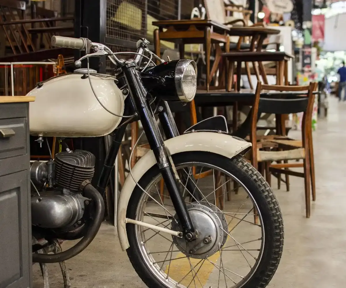 Vintage motorcycle parked indoors among furniture in a shared storage-style space without a garage