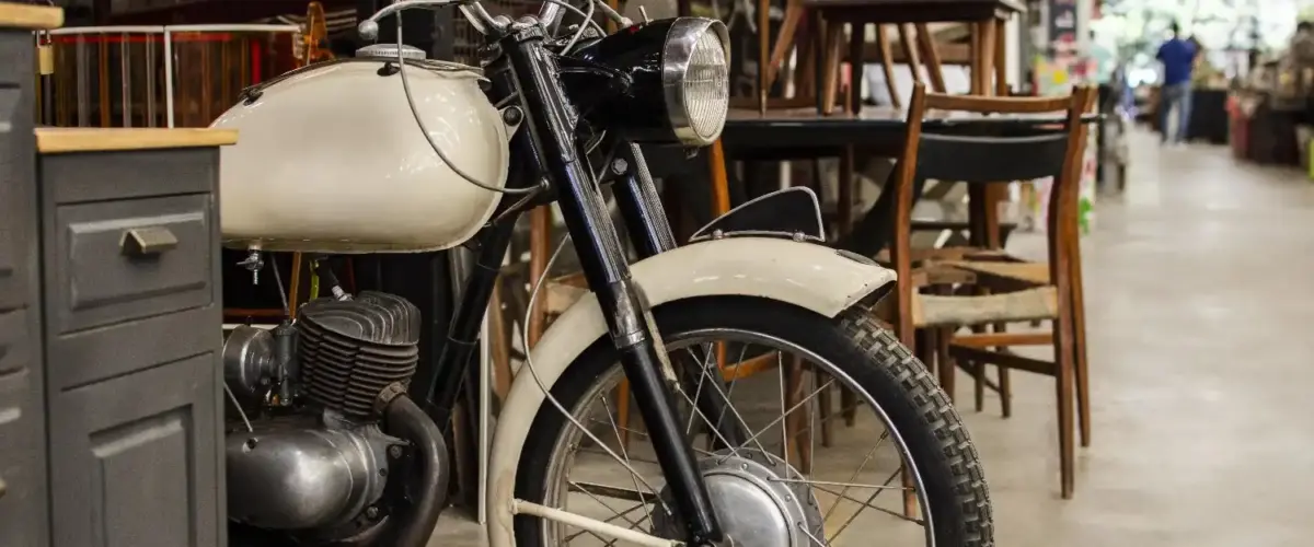 Vintage motorcycle parked indoors among furniture in a shared storage-style space without a garage